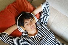Middle-aged woman listening to soothing music with headphones lying on her sofa. Female in her 50s